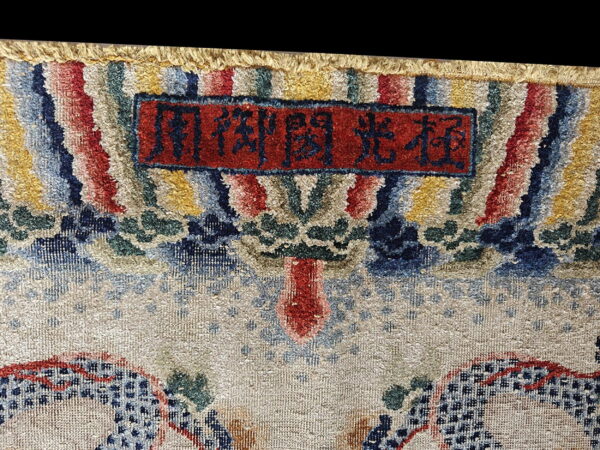 High-pile rug detail shows a colorful border, a red cartouche with script, and a beige patterned field.