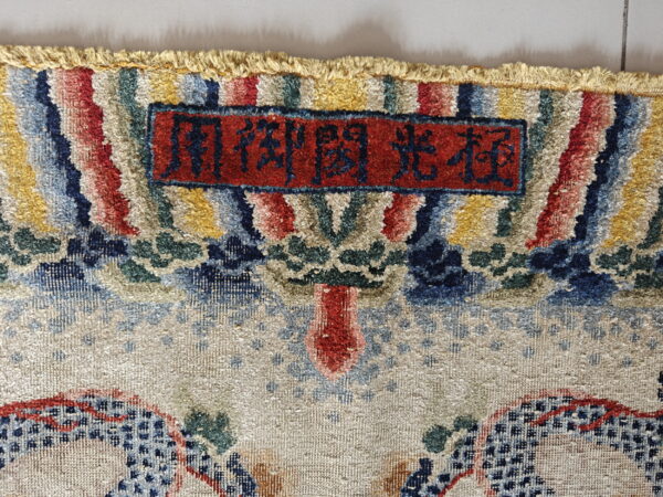Textured, multicolored rug header showing fringe and a red woven label with blue inscription.