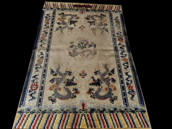 Intricate beige rug featuring blue dragon motifs, dark blue frame, and multicolored striped ends.