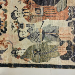A low-pile rug shows a complex pattern in beige, rust, olive green, and dark blue colors.