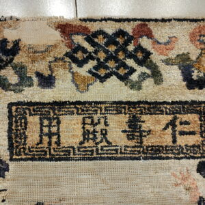 Textured beige rug detail displaying black characters within a rectangular border and a geometric knot motif.