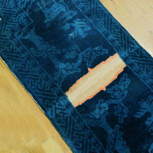 Deep indigo runner with light blue animal pattern and geometric border on wood planks, showing exposed tan foundation.