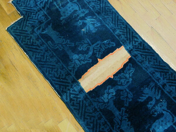 Deep indigo runner with light blue animal pattern and geometric border on wood planks, showing exposed tan foundation.