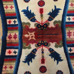 Cream rug detail showing stylized blue fish motifs, rust ground, and multicolored borders on wood plank flooring.