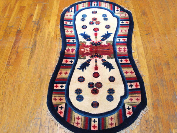 Contoured rug with a cream center, navy border, and colorful striped pattern lies on plank hardwood flooring.
