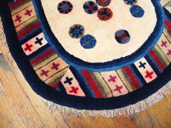 Rounded rug detail showing a cream field, navy blue edge, multicolored striped border, and tassels on wood floor.