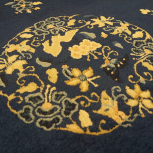 A deep blue rug featuring a vibrant yellow, stylized floral medallion and decorative vine motifs.