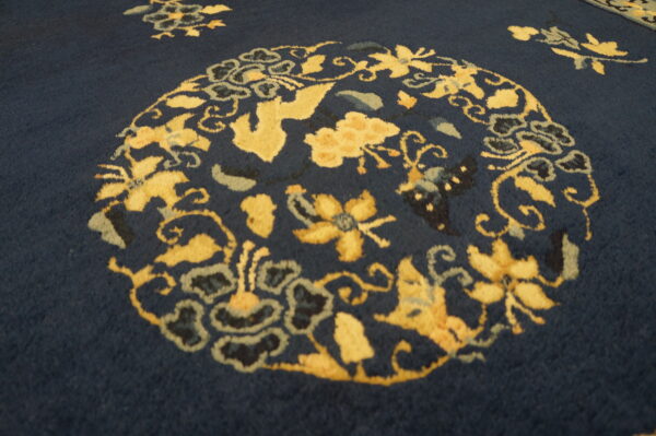 A deep blue rug featuring a vibrant yellow, stylized floral medallion and decorative vine motifs.
