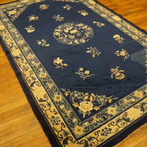 Deep blue floral area rug with detailed beige borders and scattered motifs rests on wood floorboards.