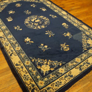 Deep blue rug with a central medallion and scattered florals, bordered in beige and light blue bands on wood flooring.