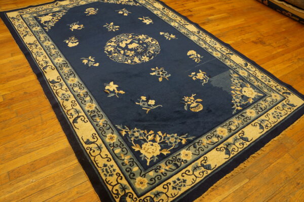 Deep blue rug with a central medallion and scattered florals, bordered in beige and light blue bands on wood flooring.
