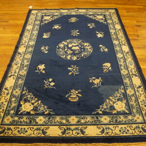 Dark blue rug with traditional cream and slate blue floral patterns and wide decorative borders on wood.