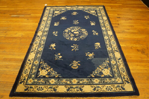 Dark blue rug with traditional cream and slate blue floral patterns and wide decorative borders on wood.