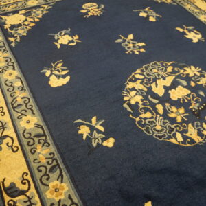 Dark blue rug with scattered yellow floral designs and a wide cream and sage patterned border on hardwood.