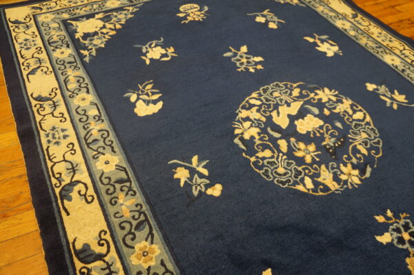 Dark blue rug with scattered yellow floral designs and a wide cream and sage patterned border on hardwood.
