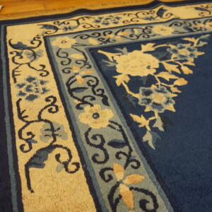 Detail shot of a plush blue rug with intricate cream and slate blue floral borders on hardwood flooring.