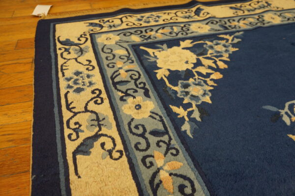 Detail shot of a plush blue rug with intricate cream and slate blue floral borders on hardwood flooring.