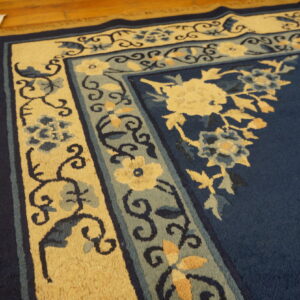 Navy blue rug with intricate pale yellow and light blue floral borders rests on polished hardwood.