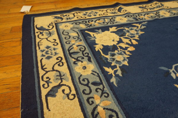 Navy blue rug with intricate pale yellow and light blue floral borders rests on polished hardwood.