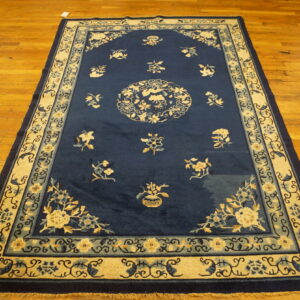 Deep blue traditional rug with ornate cream and teal floral patterns rests on golden hardwood planks.