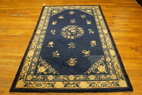 Deep blue traditional rug with ornate cream and teal floral patterns rests on golden hardwood planks.