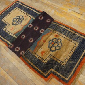 Navy, beige, and orange geometric rug, partially folded to reveal a dark center panel, resting on wood planks.