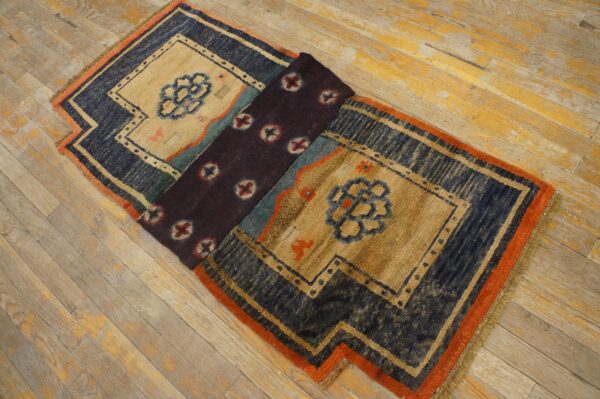 Navy, beige, and orange geometric rug, partially folded to reveal a dark center panel, resting on wood planks.