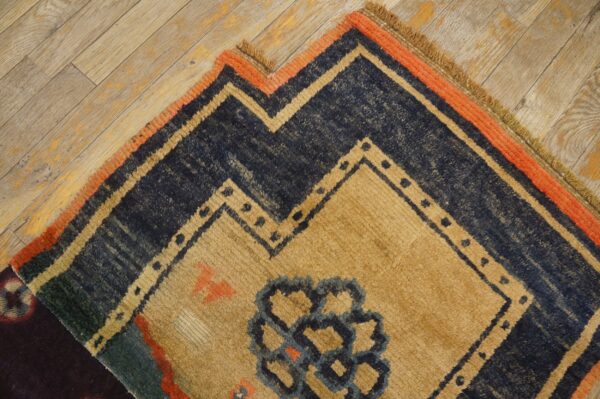 Rustic rug featuring a navy blue and tan stepped geometric pattern with an orange border on wood planks.