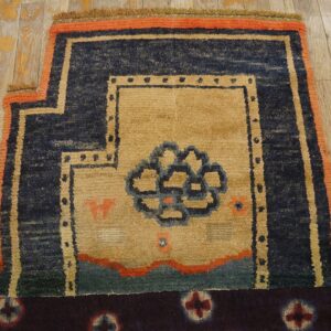 Textured tan rug featuring a blue central motif and thick navy and orange geometric borders on wood flooring.