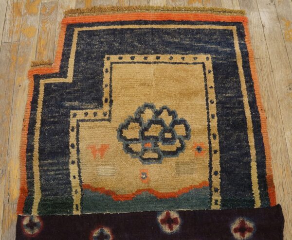 Textured tan rug featuring a blue central motif and thick navy and orange geometric borders on wood flooring.