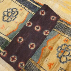 A beige, navy, and teal high-pile patterned rug is partially folded, revealing a dark purple section on wood flooring.