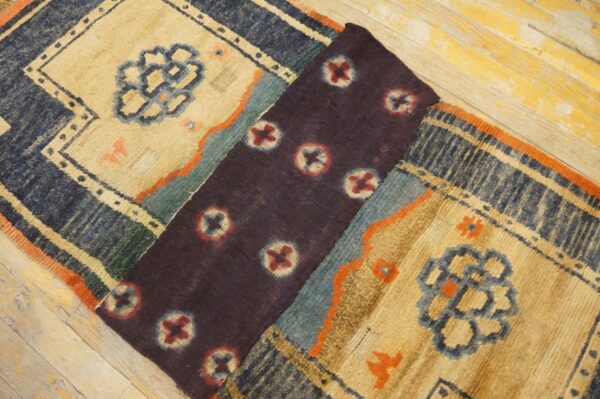 A beige, navy, and teal high-pile patterned rug is partially folded, revealing a dark purple section on wood flooring.