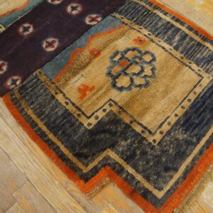 Highly textured rug segment in tan, navy, and purple patterns with an orange border, set on wood flooring.