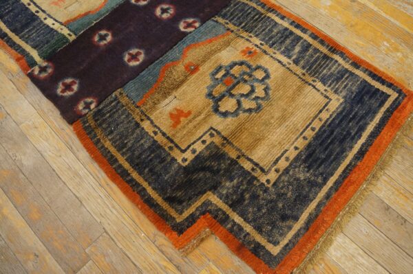 Highly textured rug segment in tan, navy, and purple patterns with an orange border, set on wood flooring.