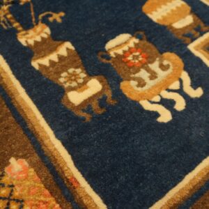 Detailed view of a rug showing brown, cream, and blue stylized vase motifs with thick pile texture.