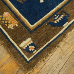 A blue and brown patterned rug corner featuring teapots rests on rustic wooden flooring.