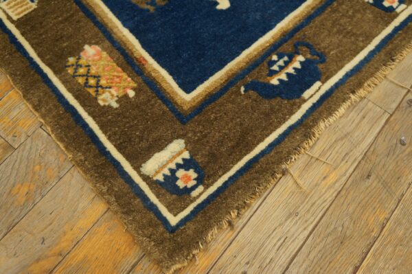 A blue and brown patterned rug corner featuring teapots rests on rustic wooden flooring.