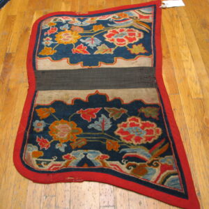 Blue, red, and gold floral textile with a central dark band rests folded on a light hardwood floor.