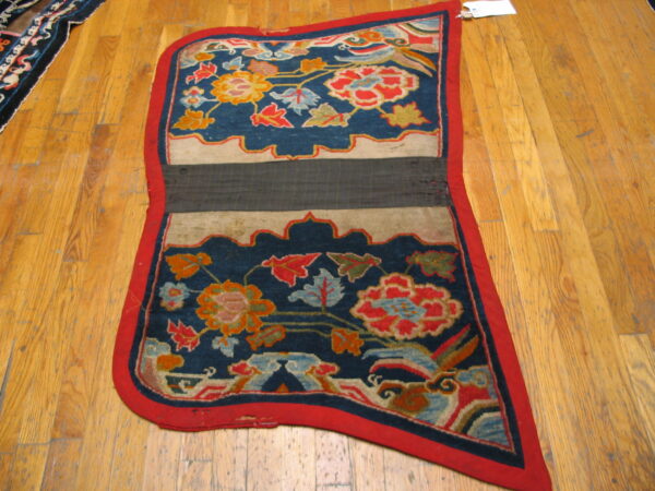 Blue, red, and gold floral textile with a central dark band rests folded on a light hardwood floor.