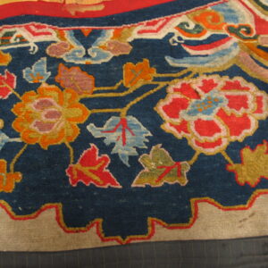 A close-up view of a deep blue rug displaying vibrant red and gold stylized floral and cloud motifs.