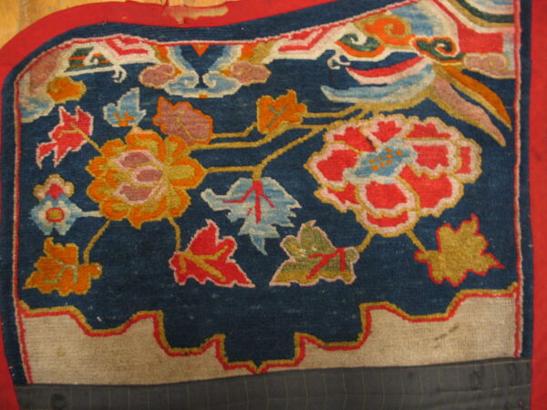 A close-up view of a deep blue rug displaying vibrant red and gold stylized floral and cloud motifs.