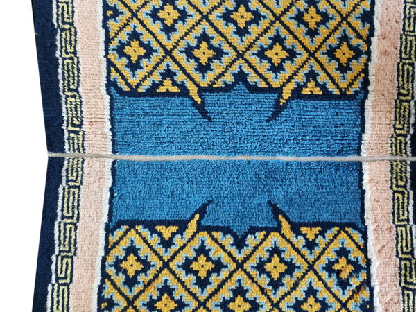 Textured rug detail with bright blue shag pile, geometric yellow diamonds, and plush pale pink borders.