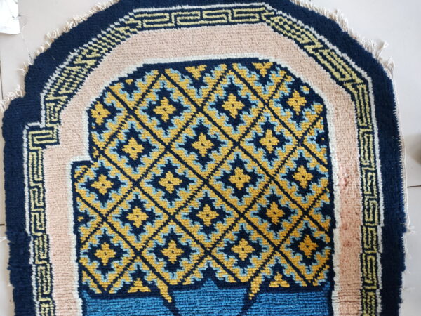 Navy, gold, and light blue rug with geometric lattice and pink borders on a light floor.