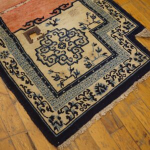Low-pile rug in cream, navy, and pale pink with stylized blue borders rests on distressed wood flooring.
