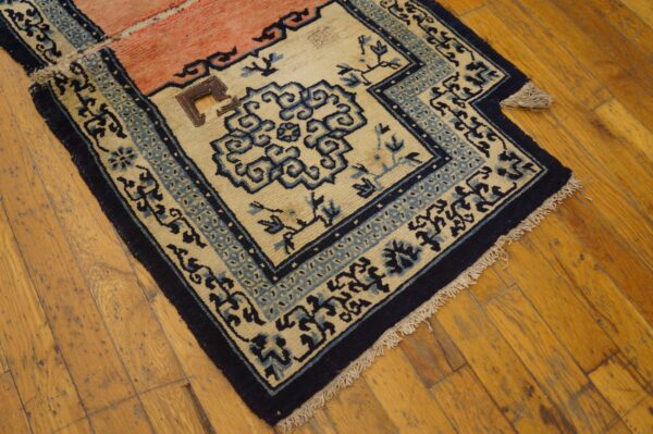 Low-pile rug in cream, navy, and pale pink with stylized blue borders rests on distressed wood flooring.