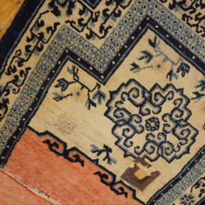 Cream, navy, and coral geometric rug showing patches rests on a plank hardwood floor.