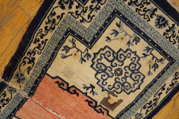 Cream, navy, and coral geometric rug showing patches rests on a plank hardwood floor.