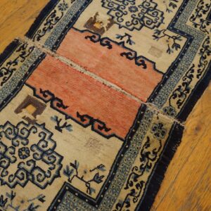 A worn rug runner in beige, dark blue, and coral features geometric patterns on honey-toned wood planks.