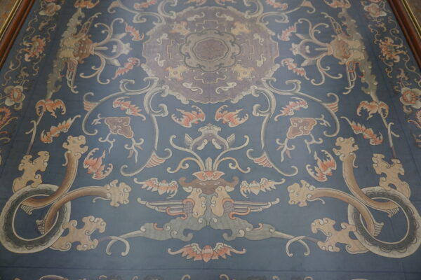 Muted blue rug with a traditional design featuring ornate dragons, scrolling vines, and flowers.