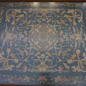 A flat, framed blue rug with an ornate pattern of dragons, phoenixes, and flowers rests on wooden floor planks.